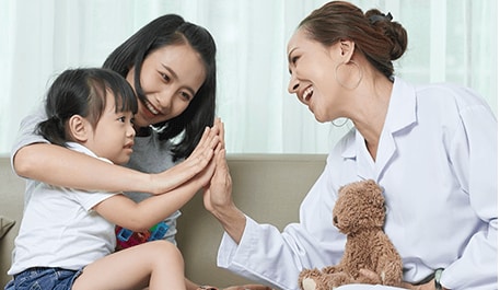 Boy sitting on his mother's lap highfiving an adult